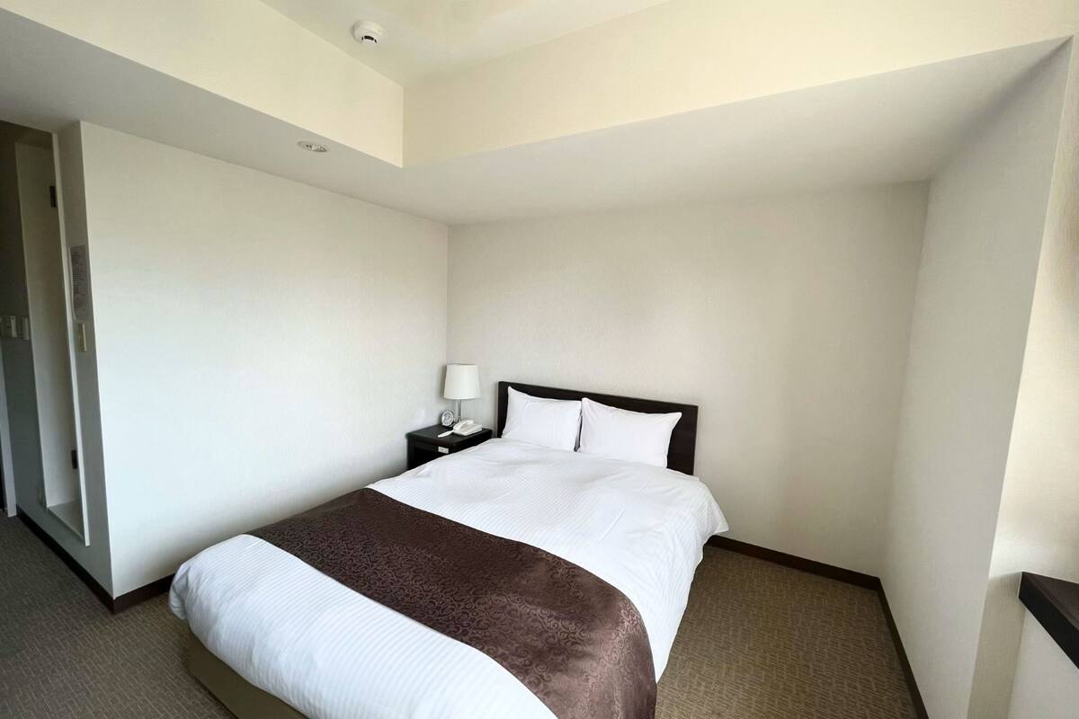 A hotel room with a large bed, a bedside table with a lamp, and a telephone.