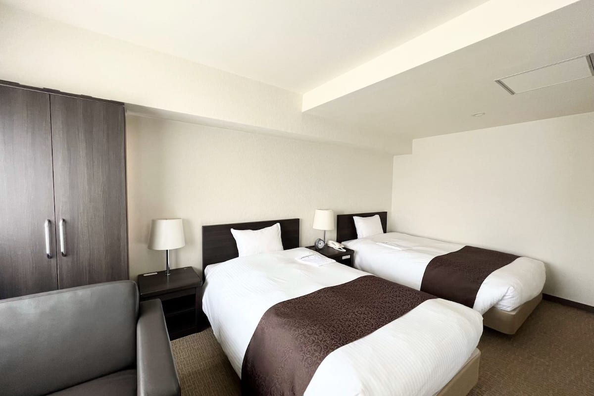 A hotel room with two beds, a wardrobe, a desk, and a chair.