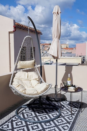 A hanging chair with cushions, a small table with a bottle and glasses, and a patterned rug on a rooftop terrace. - Venetian Owl, 1min To Lighthouse (Chania)