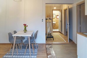 A modern interior with a dining table, chairs, a vase of flowers, and a hallway leading to a bathroom with a wooden floor and a mirror. - Venetian Owl, 1min To Lighthouse (Chania)