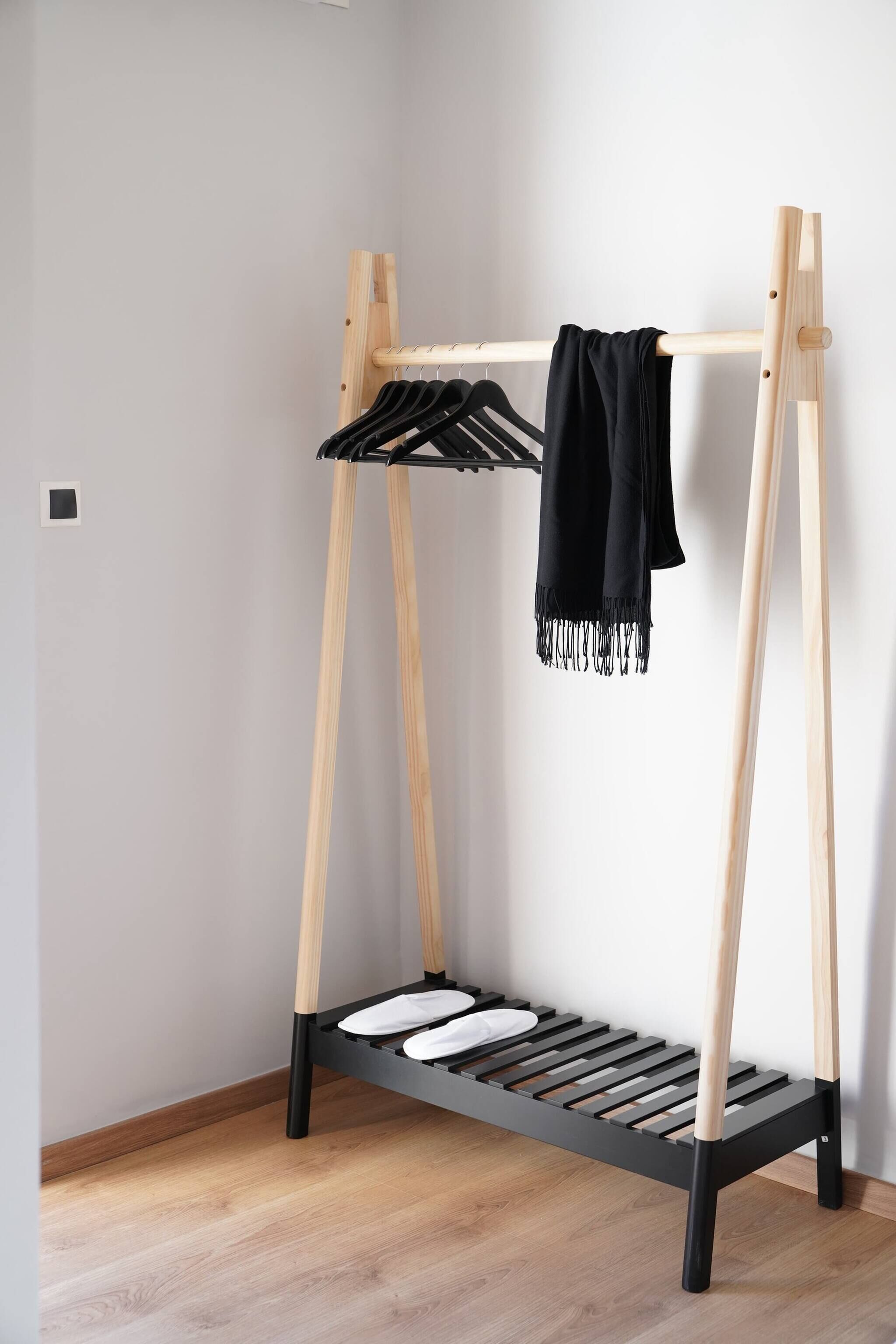 A wooden bed frame with a black mattress and a black towel hanging on a wooden rack.