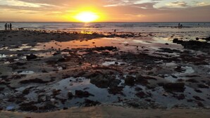 A beach scene with a sunset, rocky shore, and people in the distance. - Casa em Paracuru Beach (Paracuru)