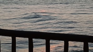 A sunset over a body of water with a wooden railing in the foreground. - Casa em Paracuru Beach (Paracuru)