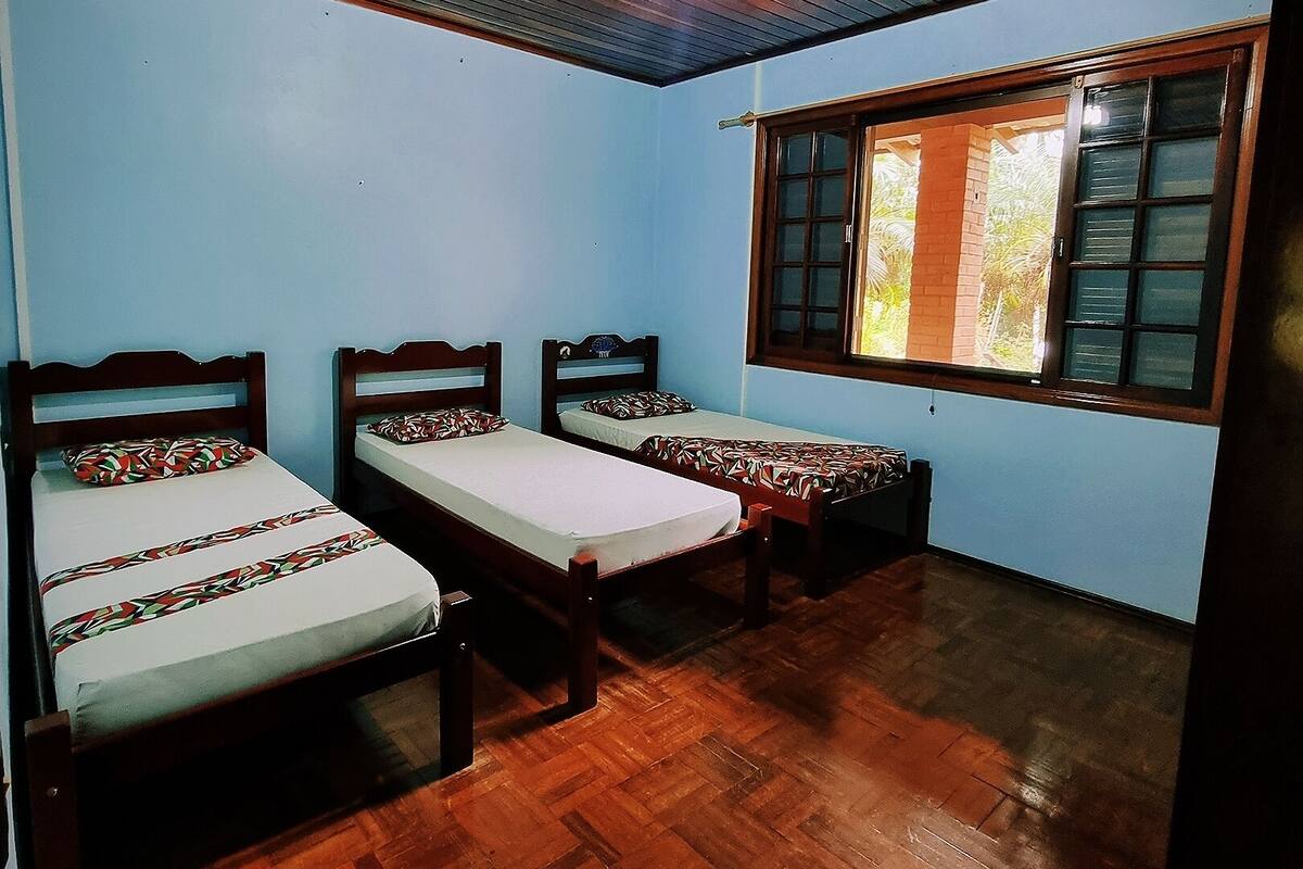 A room with three wooden beds, a window with a view of greenery, and a wooden ceiling.