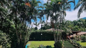 Piscina com azulejos de pedra, rodeada por vegetação exuberante e palmeiras.
