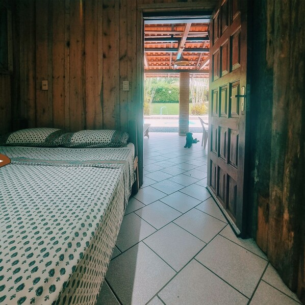 Una habitación de madera con una cama, una mesita y vistas a un jardín por una puerta abierta.