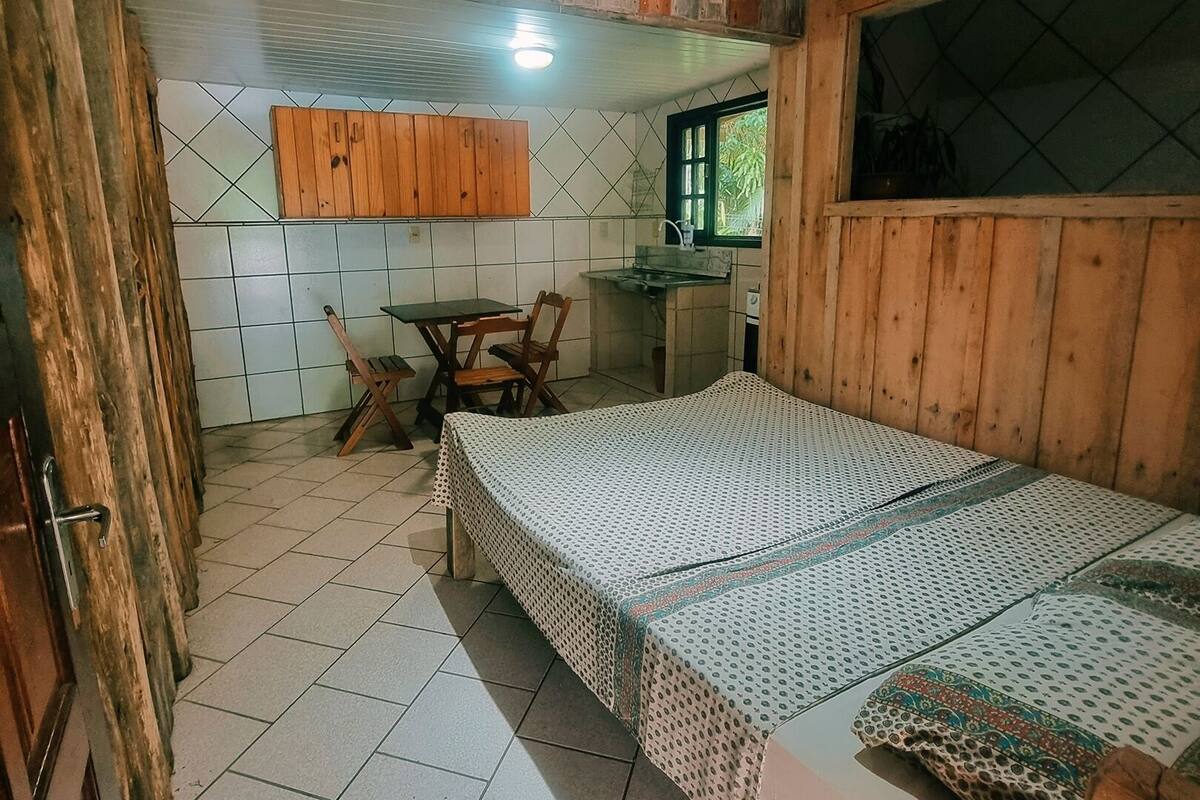 A small, rustic room with a bed, a wooden table, and a kitchenette.