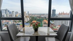 Una habitación con una mesa, dos sillas, una planta en maceta y vistas a un paisaje urbano a través de amplios ventanales.
