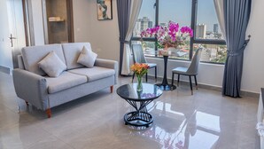 Una sala de estar moderna con un sofá gris, una mesa de centro de vidrio y vistas de la ciudad a través de amplios ventanales.