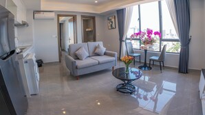 Una sala de estar moderna con un sofá gris, una mesa de comedor con dos sillas, una mesa de centro de vidrio y un ventanal con cortinas.