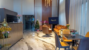 Un moderno vestíbulo de hotel con un mostrador de recepción, una zona de estar con sofá y sillones, una mesa de comedor y una pantalla de televisión que muestra 'Parc 21'.