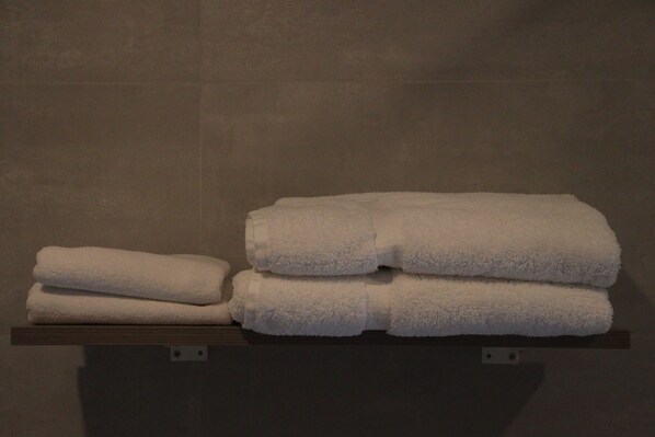 A stack of white towels on a wooden shelf against a tiled wall.