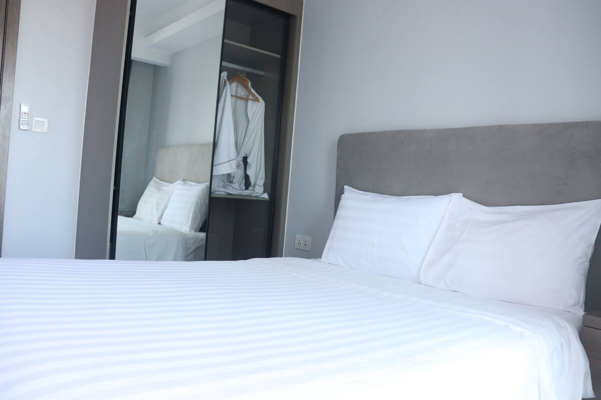 Ein Hotelzimmer mit einem ordentlich bezogenen Bett, einem grauen Kopfteil und einem begehbaren Kleiderschrank mit Kleiderstange.