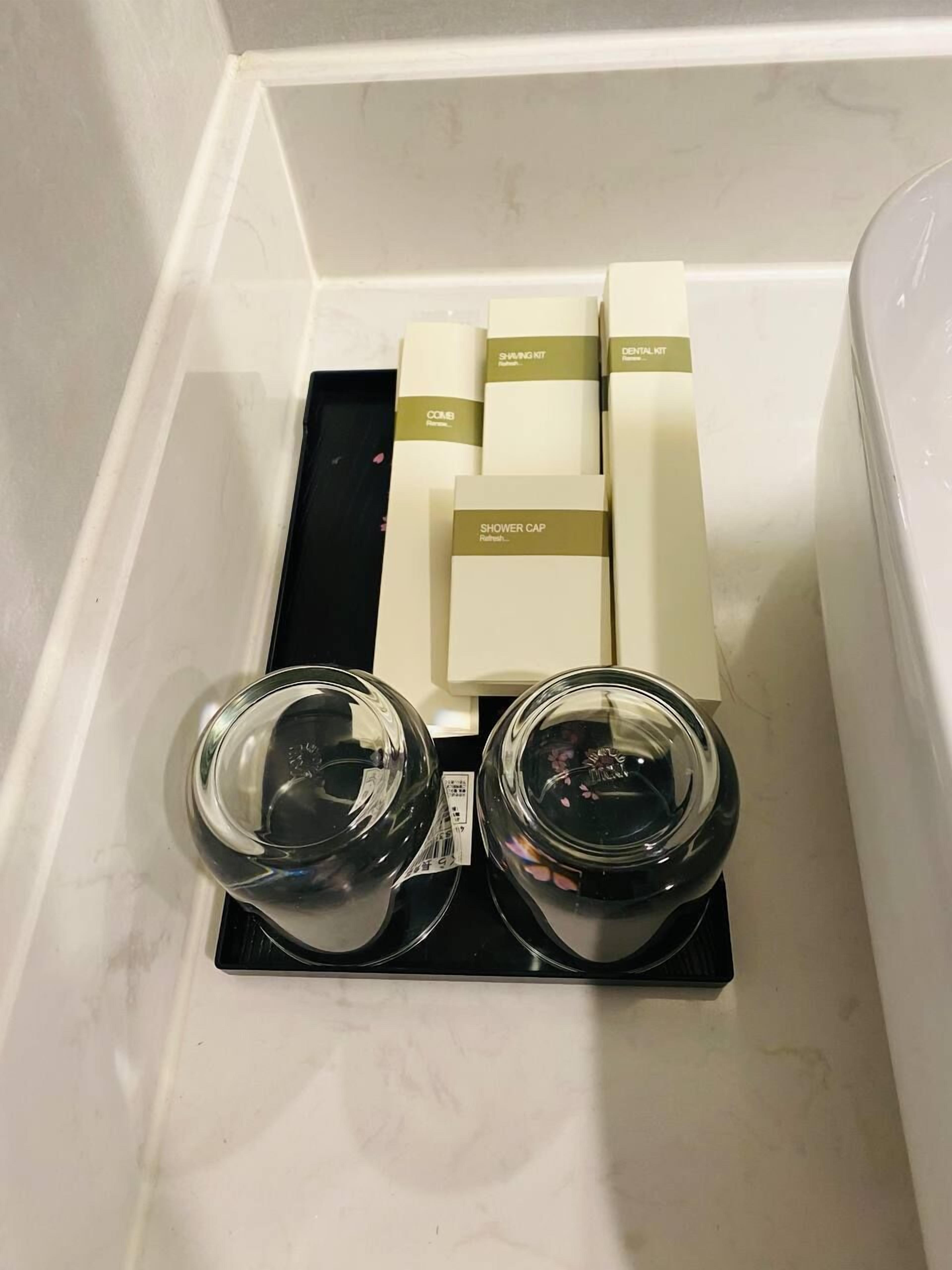 A bathroom with a white bathtub, a black tray holding two glass jars, and three toiletries in a beige box set.