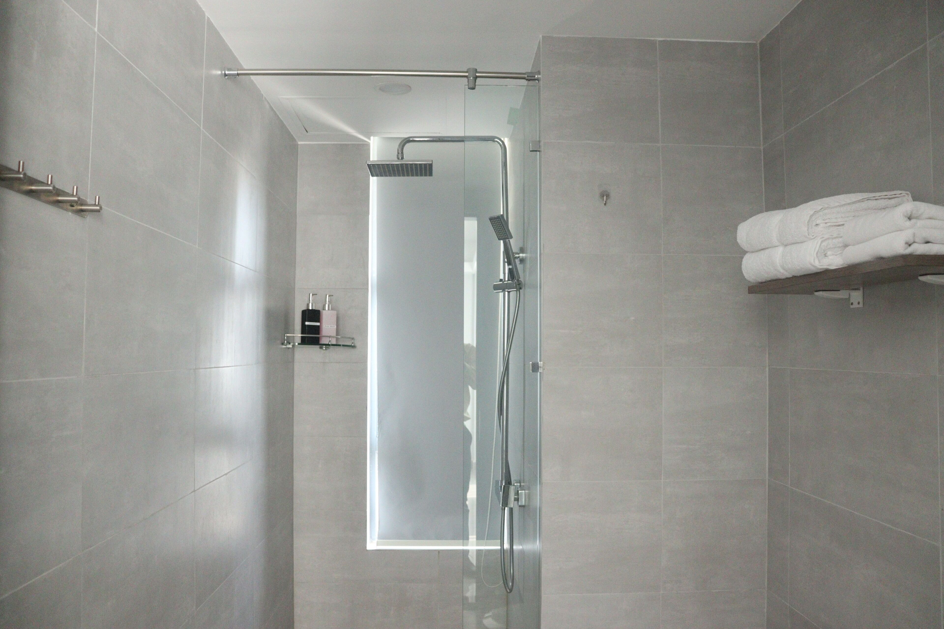Une salle de bain moderne avec une douche à parois de verre, un porte-serviettes et une étagère où sont pliés les serviettes.