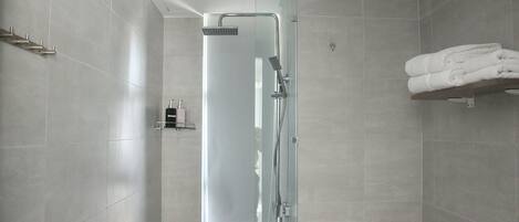 A modern bathroom with a glass-enclosed shower, a towel rack, and a shelf with folded towels.