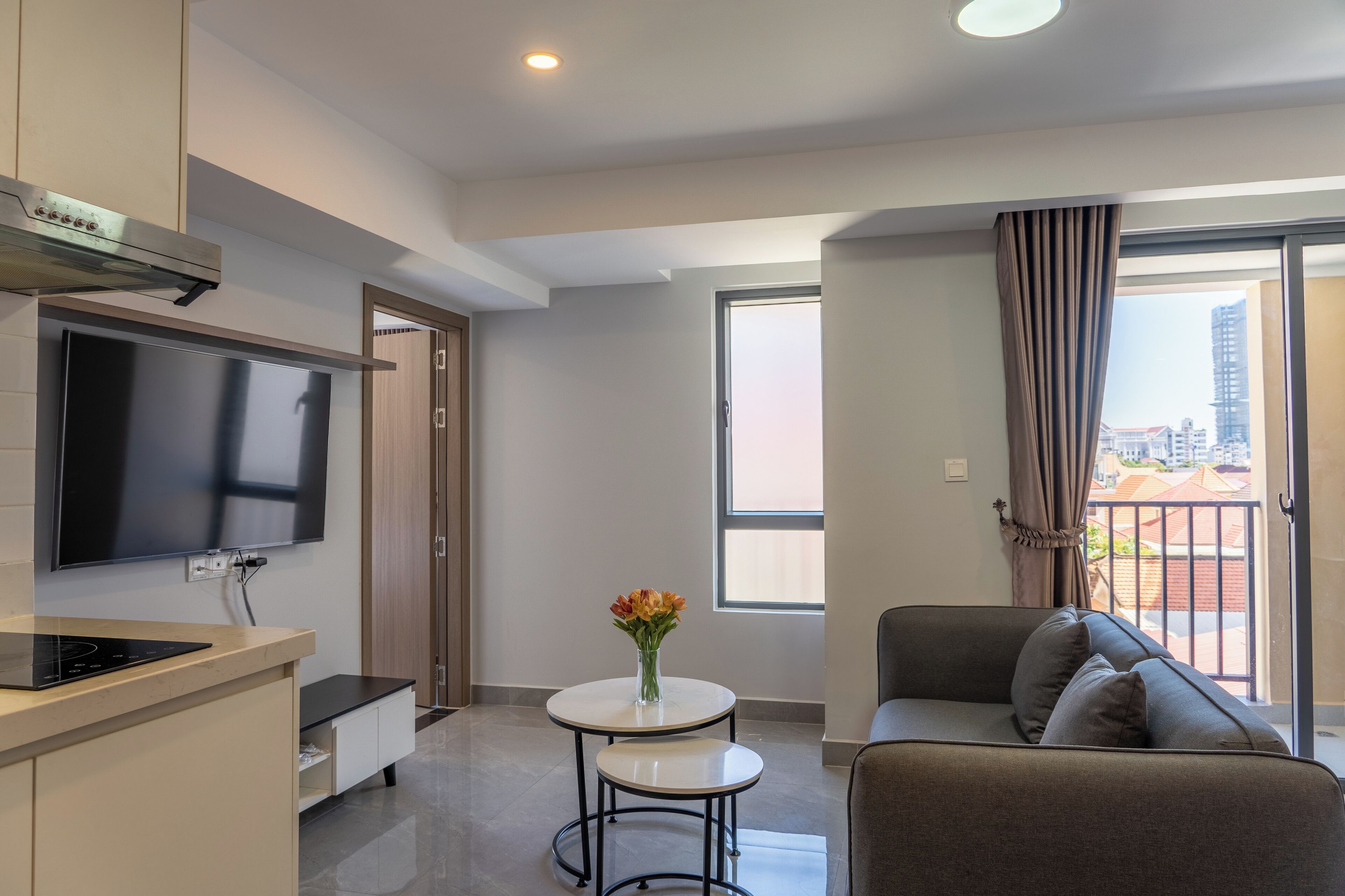 Una sala de estar moderna con un televisor de pantalla plana, una mesita redonda con un jarrón de flores y un sofá.