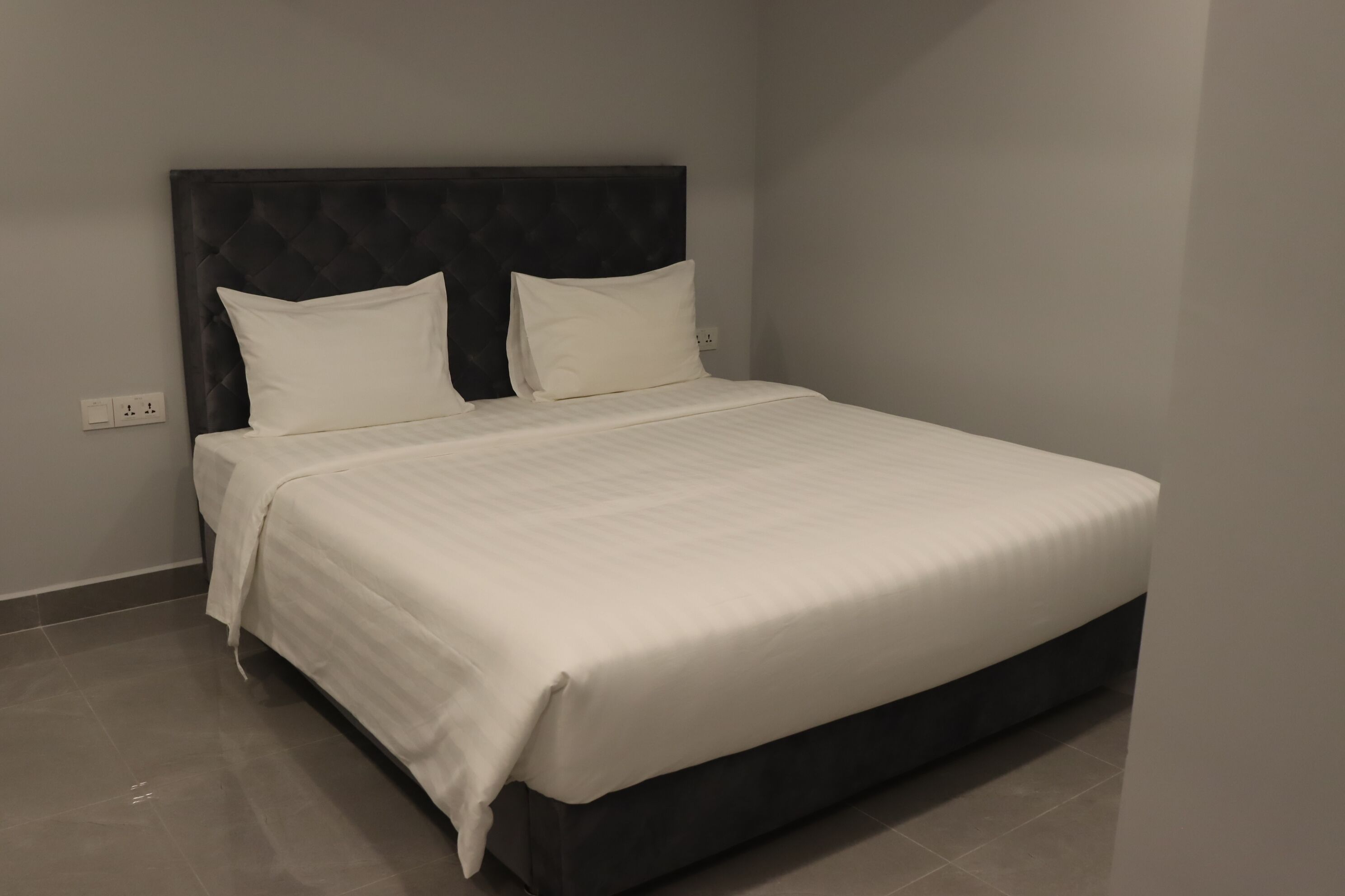A neatly made bed with a dark headboard and white bedding in a modern room with a tiled floor.