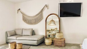 A living room with a sofa, a large mirror, a hanging macrame wall hanging, and wicker baskets. - Cozy Studio In La Veleta (Tulum)