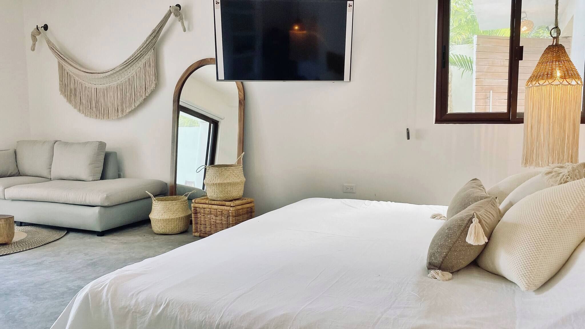 A bedroom with a large bed, a sofa, a hammock, a TV, and a hanging light fixture.