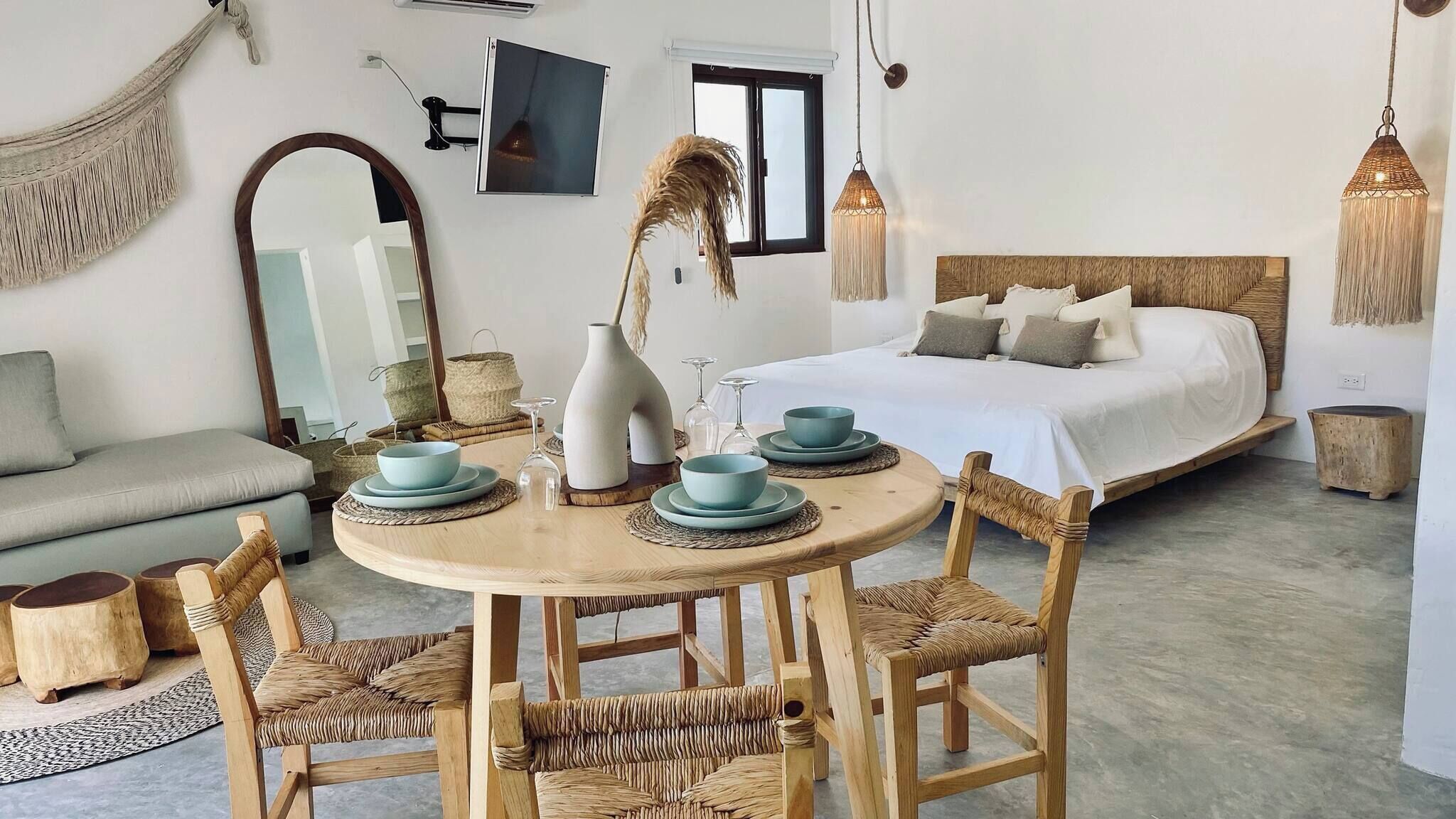 Une pièce comprenant un lit, une table ronde en bois avec des chaises, un canapé et un grand miroir.