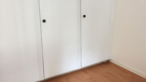 Habitación con piso de madera y paredes blancas, que incluye un armario grande con dos puertas y una pequeña.