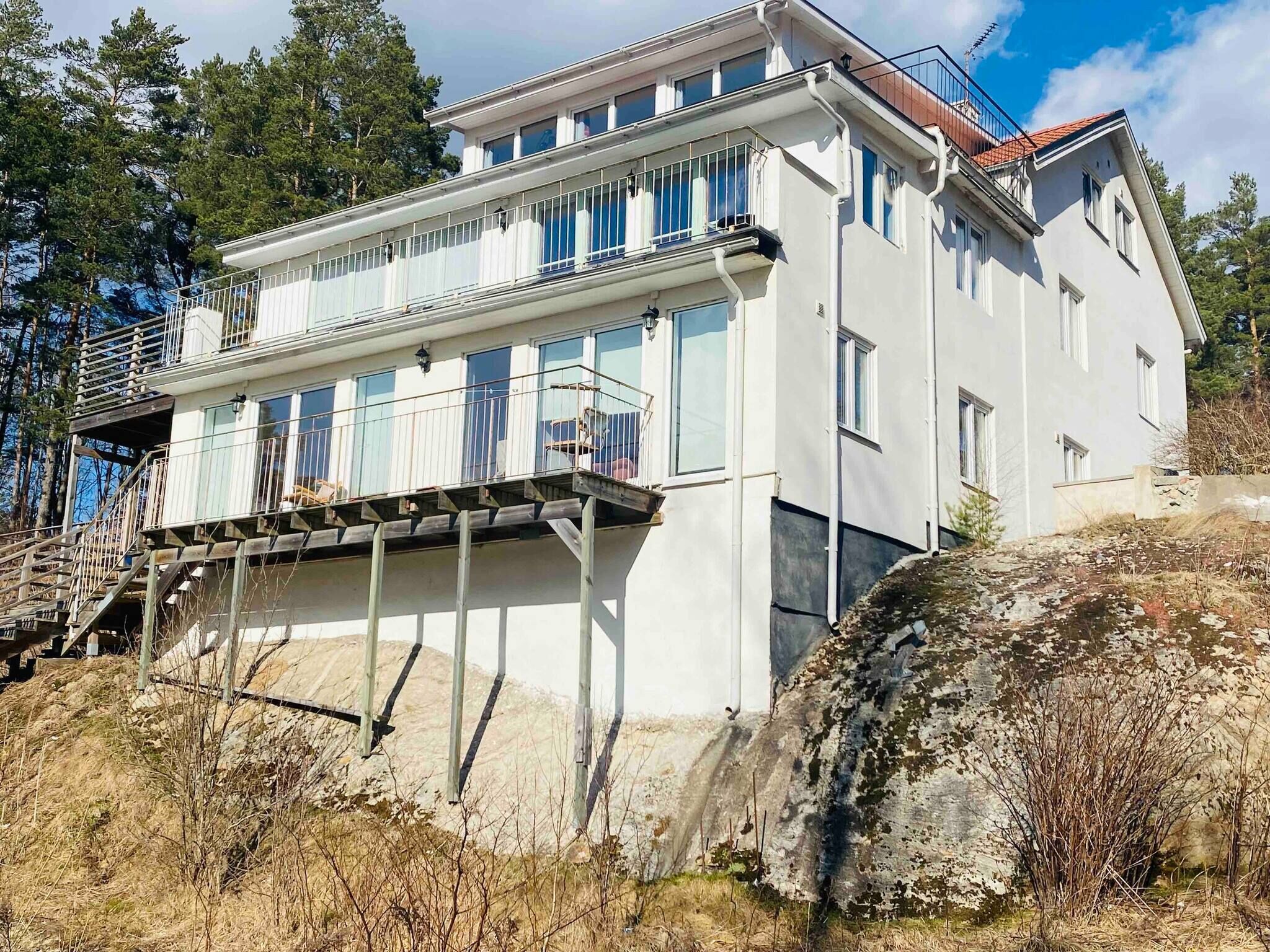 A two-story building with a balcony on the upper floor, surrounded by trees and a rocky hillside.