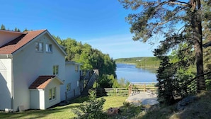 A white building with a red roof, a wooden deck, and a view of a lake. - Bjurvik's Villa - Flat 2 - Business Customers Only (Flen)