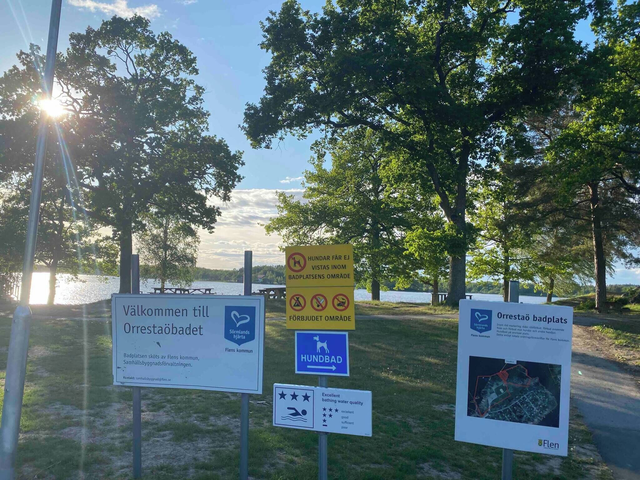 A signboard with multiple informational signs, including a welcome sign, a dog-friendly area, and a water quality rating.