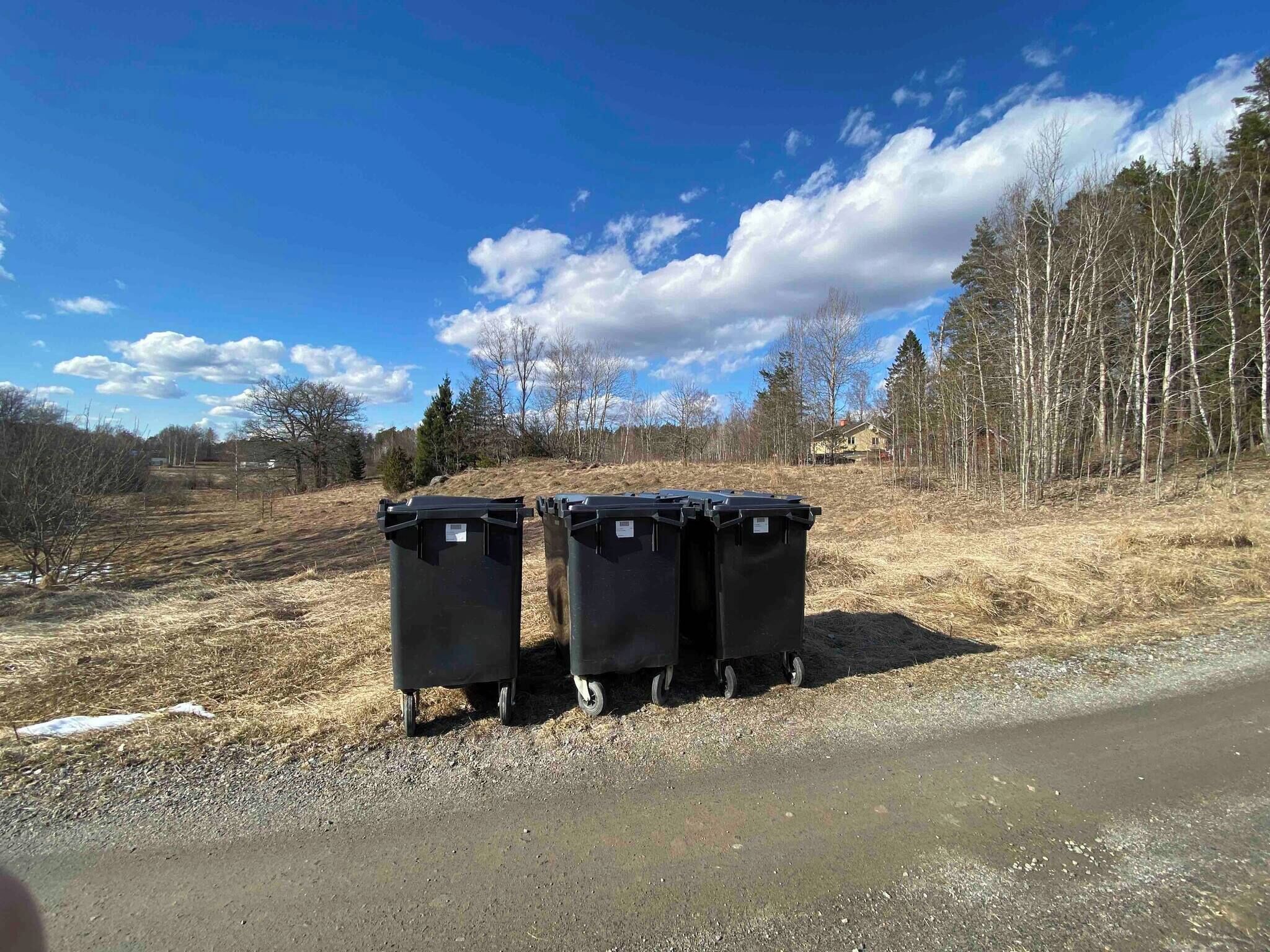 Dos contenedores de basura negros sobre ruedas en un camino de grava.