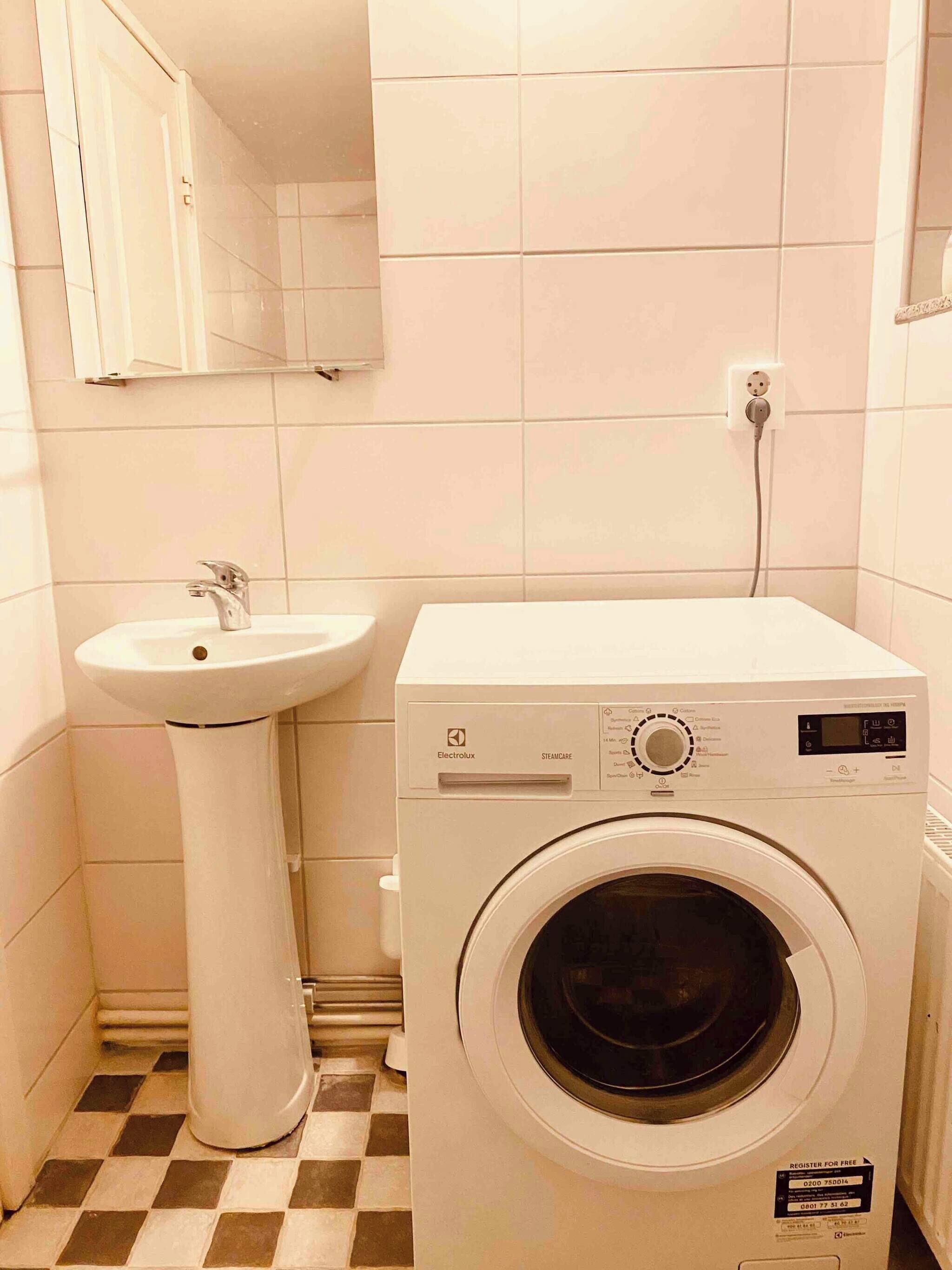 A compact laundry room with a washing machine and a pedestal sink.
