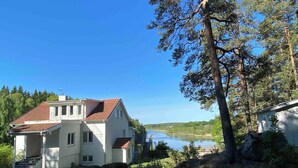 Une maison à deux étages, avec un toit recouvert de tuiles rouges, un balcon et une vue sur un lac.