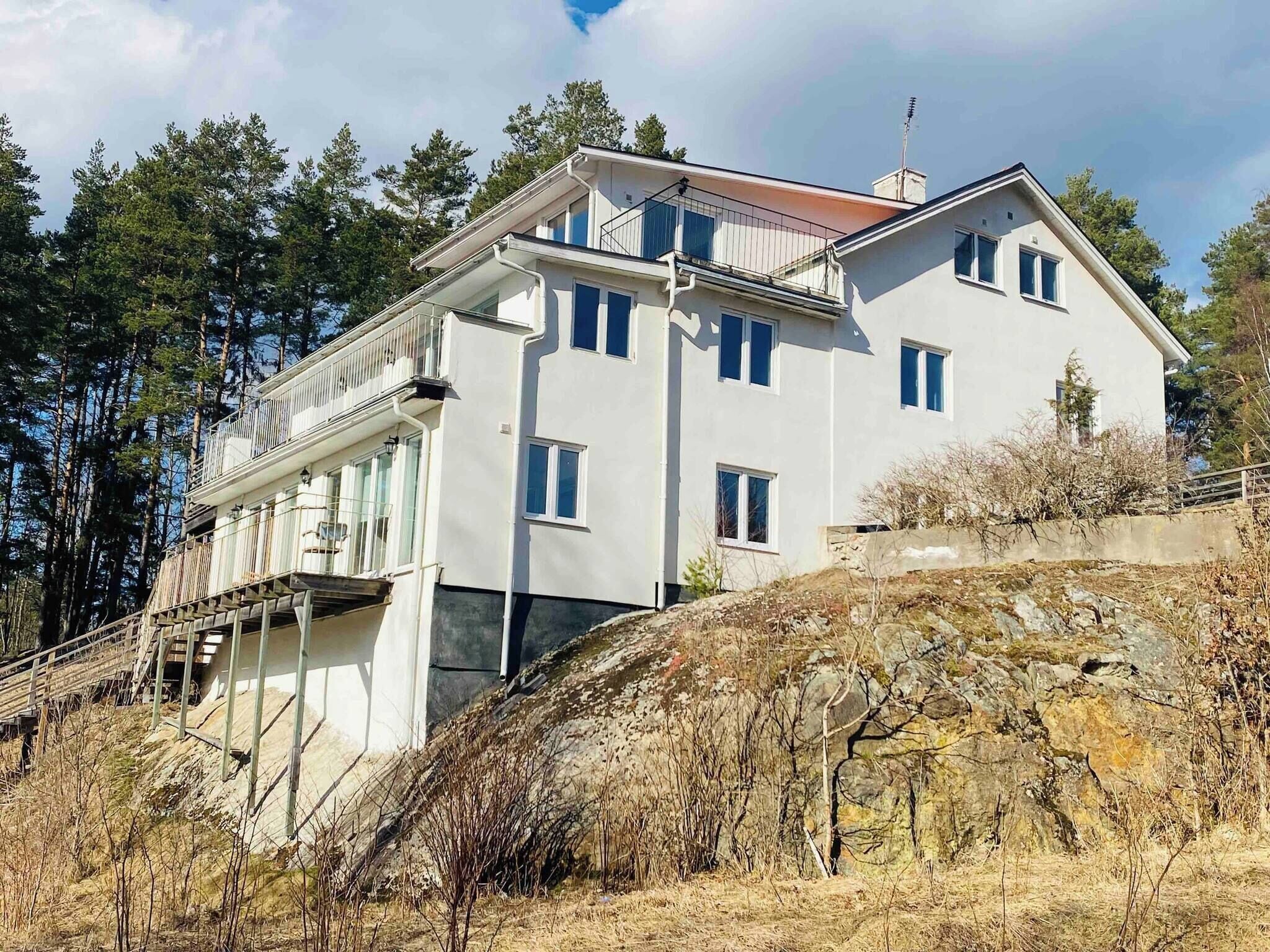 A two-story building with a balcony, situated on a hillside with trees in the background.