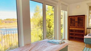 Une chambre avec une grande fenêtre, une armoire en bois et un lit recouvert d’une couverture à motifs.