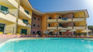 A swimming pool with a building featuring multiple balconies and a clear blue sky.