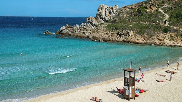 A beach with clear turquoise water, rocky cliffs, and a lifeguard tower.