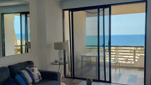 Ein modernes Wohnzimmer mit Sofa, Couchtisch und Meerblick durch große Schiebetüren.