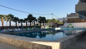 Une piscine entourée de bâtiments, agrémentée de chaises longues et de palmiers.