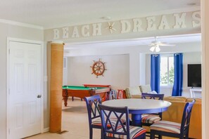 Un salon comprenant une table de billard, une table ronde avec des chaises, un canapé et une horloge murale.