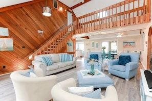 Un vaste espace de vie doté d’un plafond haut et de poutres en bois, d’un escalier et d’un coin repas aménagé avec des meubles modernes.