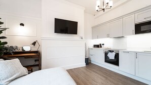 A modern bedroom with a bed, bedside table, and a desk with a lamp. - Luxury Apartment In The Heart Of Hoylake (Wirral)