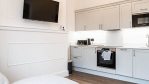 A modern kitchen with white cabinetry, a built-in oven, and a flat-screen TV mounted above the counter. - Luxury Apartment In The Heart Of Hoylake (Wirral)