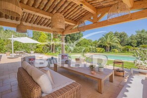 An outdoor patio with wicker furniture, a wooden table, and hanging wicker lamps. - Magnificent villa in Grimaud (GRIMAUD)