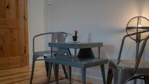Ein kleiner, rustikaler Raum mit Holzboden, einem Metalltisch und zwei Stühlen sowie einer einzelnen Blumenvase.