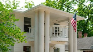 Ein zweistöckiges Haus mit Balkon, Steinpfeilern und einer amerikanischen Flagge.