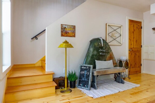 A wooden staircase leading to a room with a green chair, a lamp, and a chalkboard sign.