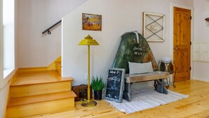 A wooden staircase leading to a room with a green chair, a lamp, and a chalkboard sign. - Downtown Historic Loop Downstairs King Free Parking (Eureka Springs)