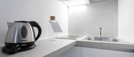 A modern kitchen with a stainless steel kettle, a sink, and a clear glass container with a cork stopper.
