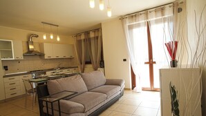 A modern kitchen with a dining area, a sofa, and a large window with curtains.