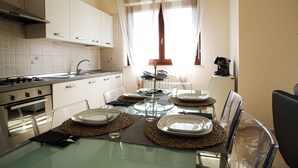 A modern kitchen with white cabinets, a glass dining table, and a window with curtains.
